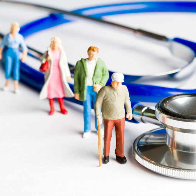Mini people figurines stand in line beside a stethoscope. -- health business coverage from STAT