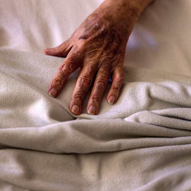 An elderly person's hand on bedsheets