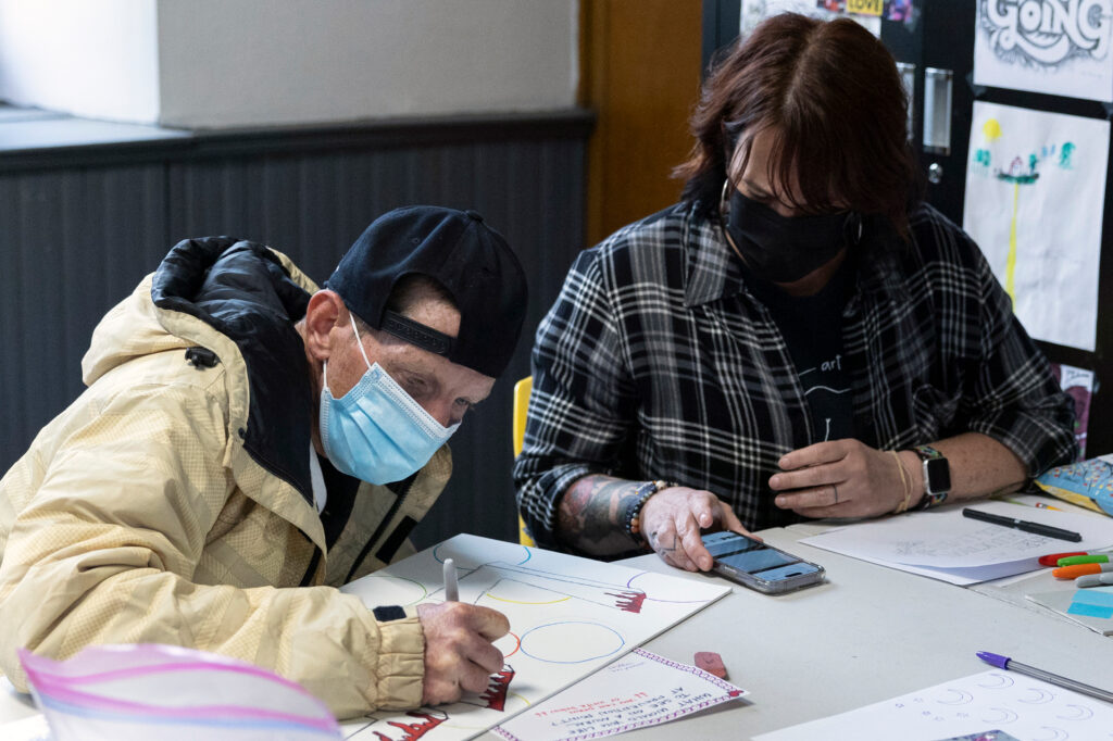Anderson (left) draws with artist Lisa Kelley, who co-hosts a biweekly art lesson at Prevention Point in Kensington, in May 2023.